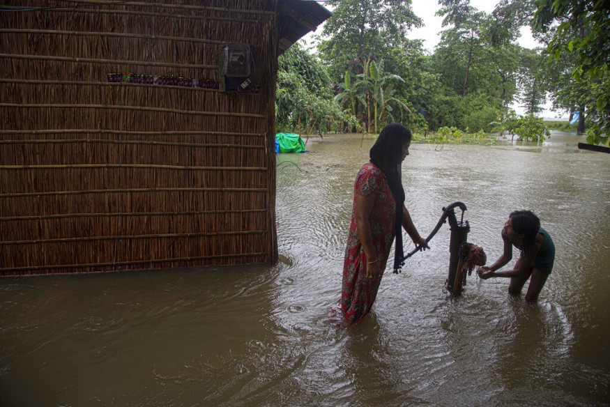 A woman helps a child with water from a hand pump half-covered in floodwaters in Morigaon district of Assam. (Image: AP)
